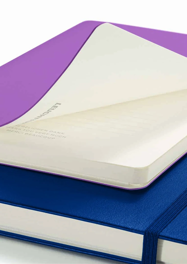 An open softcover notebook resting on a hardcover notebook, showing flexible and firm cover construction